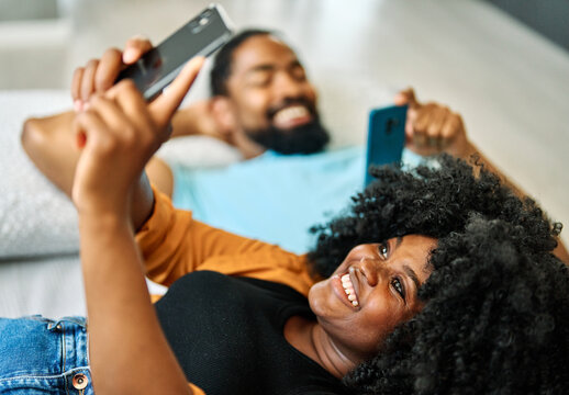 Portrait of a young happy couple texting and using a smartphone at home. Girlfriend and boyfriend bonding, love concept - Powered by Adobe
