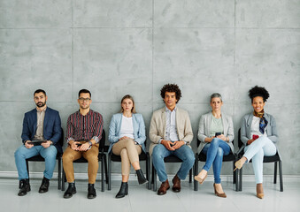 Group of young businss people sitting in chairs and waiting for an interview using phones and...