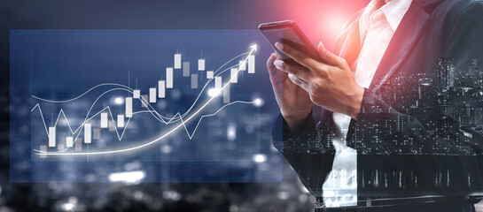 A businessman is intently using a smartphone while analyzing financial graphs with city lights...