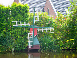 Rustic dutch scale windmill surrounded by lush greenery and a serene waterway reflects peaceful rural charm