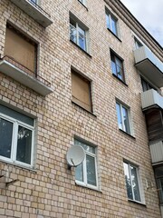 Fototapeta premium Facade of a Soviet-era residential apartment building with several boarded-up windows, satellite dish, and visible balconies. The wall is covered with aged beige ceramic tiles