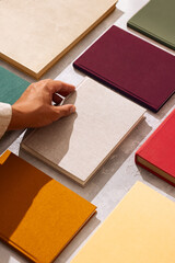 Hand picking a linen-covered book from a flat lay of colorful hardcovers on a textured background.