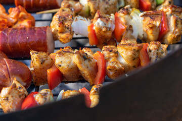 Grilled chicken and vegetable skewers cooking on barbecue over hot charcoal, close-up of kebabs with onion, red pepper, and sausage on outdoor grill.