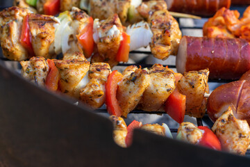 Grilled chicken and vegetable skewers cooking on barbecue over hot charcoal, close-up of kebabs with onion, red pepper, and sausage on outdoor grill.