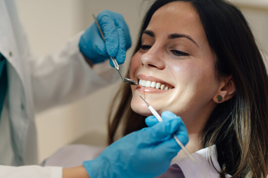 Dentist examining teeth of smiling female patient in dental clinic