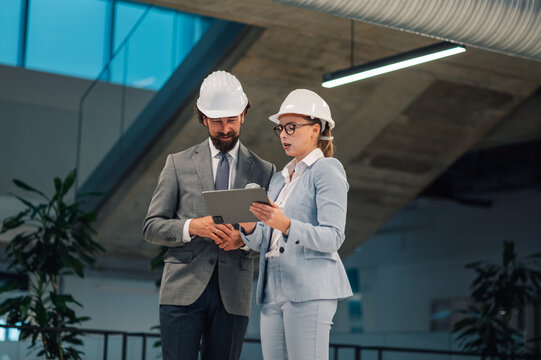 Architects using digital tablet discussing blueprint in modern building - Powered by Adobe