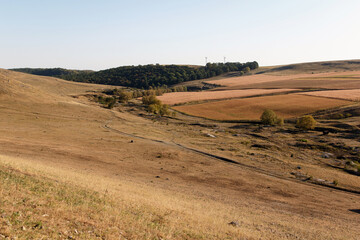 A vast, dry landscape with rolling hills and sparse vegetation. The terrain features brown grass...