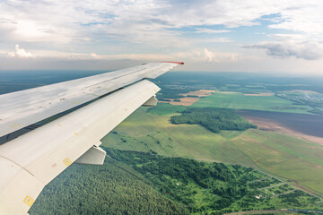 View of airplane wing, blue skies and green land during landing. Airplane window view.