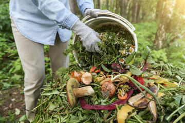 Composting, separate waste collection concept. Zero waste, compost. Compost heap pile with bio waste. Farmer hands put weeds grass plants, vegetable fruit scraps from bucket in compost close up