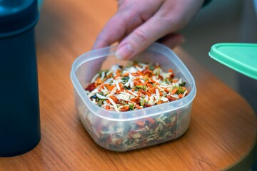 Woman's hand holding a plastic container with dried vegetables for cooking, meal prep and healthy...