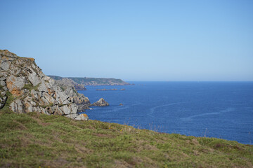 Fototapeta premium A view from a grassy clifftop on the Brittany coast, looking out over the sea towards a distant headland.