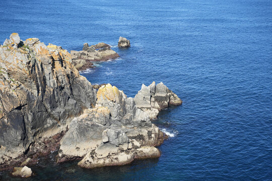 An elevated view of a rugged, rocky headland extending into the deep blue sea on the coast of Brittany, France.