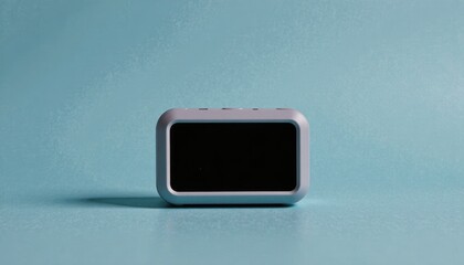 A contemporary digital smart clock with a minimalist grey casing and a blank screen, resting on a serene light blue surface for a modern, clean aesthetic.