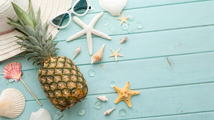 Ripe pineapple sunglasses straw hat and seashells on light blue wooden background fruit tropical
