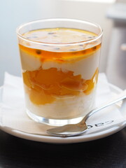 Delightful mango passionfruit dessert served in clear glass with spoon on table in cozy cafe