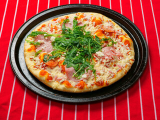 A pizza with ham and spinach on a black tray. The pizza is sitting on a red and white stripe table...