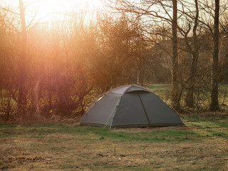 Home less family tent in a park with town houses in the background behind trees. High cost of living. Poor and rich concept. Social imbalance and issue. Warm sun flare. Living in harsh conditions.