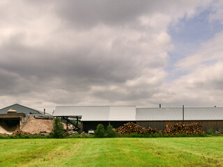 Obraz premium A large wood processing factory building with a lot of wood stack and a huge pile of sawdust. The sky is cloudy and the mood of the image is somewhat somber.