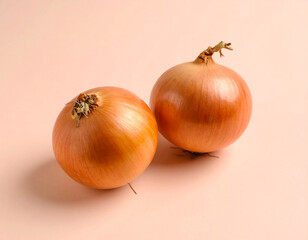 Two golden onions with dried stems on a soft pink surface, studio shot