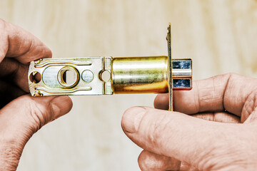 Hands holding door latch with spring mechanism showing intricate design and metallic finish