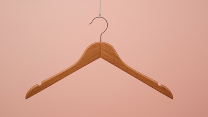 Wooden Clothes Hanger with Metal Hook Suspended Against Soft Pink Background