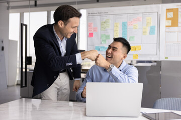 Hispanic and Chinese businessmen greeting each other in modern boardroom, exchanging fist bump, gesture of mutual respect, showing team spirit, sense of unity and togetherness. Teamwork, partnership