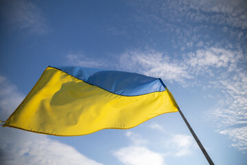 The flag of Ukraine waves in the wind, showing its blue and yellow stripes, against a blue sky with...