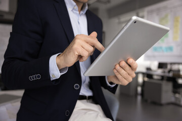 Close up cropped view of businessman using digital tablet in modern office, reviewing financial data or preparing online presentation for upcoming meeting, making data analysis or responding to client