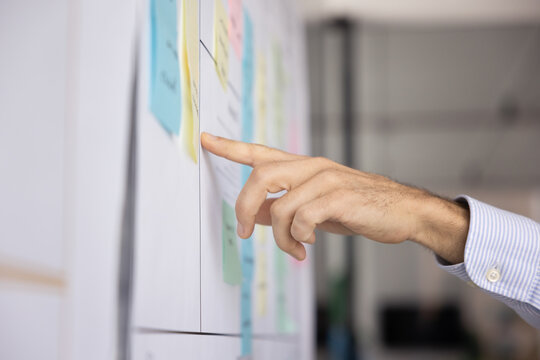Close up man hand points at whiteboard covered with organized colorful sticky notes, busy in planning or analysis. Project management, visual methodology, task tracking, work or deadlines prioritizing