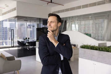 Pensive middle-aged Hispanic businessman dressed in formal attire stands in office, looks aside...
