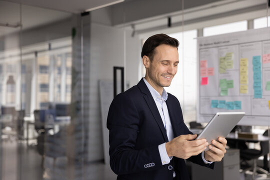 Smiling Hispanic businessman accessing information, lead digital communication using tablet, reviewing data or reports, chatting with colleagues or clients via email, messaging or video conferencing - Powered by Adobe