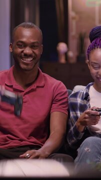 Casual happy love couple of young african woman and man holding gamepads wireless devices playing jostick console videogame on TV. Family portrait.