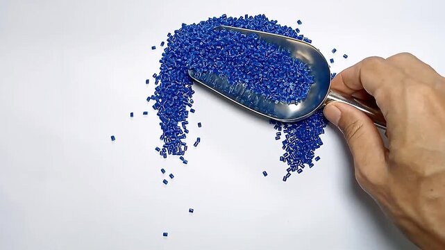 Pouring dark blue masterbatch granules into a white background medium with a stainless scoop, suitable for videography design of plastic industry company profiles	
