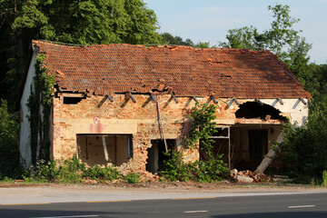 A derelict brick house with a heavily damaged tiled roof shows collapsed walls and extensive...