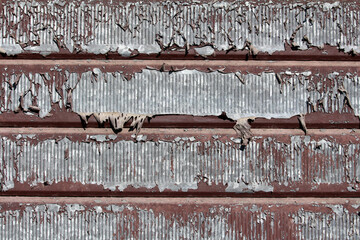 Detailed view of old corrugated metal siding shows brown substrate and extensive peeling gray...