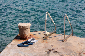 Two pairs of rubber slides rest on a weathered concrete pier next to a metal swim ladder and a...