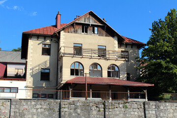 A traditional multi-story house features arched windows, a red metal roof, weathered exterior, and...
