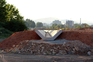 A V-shaped precast concrete drainage channel is installed in a trench amid red earth, rocks, and...