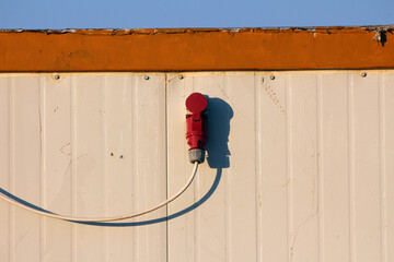 A heavy-duty red electrical power plug is securely installed on a beige metal wall, with a thick...