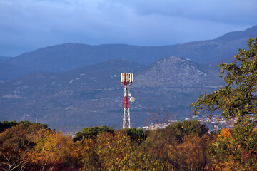 A tall cellular communication tower equipped with antennas rises above a forested landscape with...