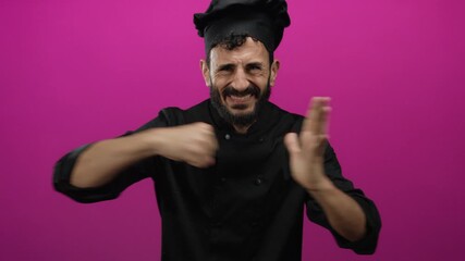 Hispanic bearded man chef gesturing aggressively in black uniform against a vibrant pink background portraying frustration and emotion.