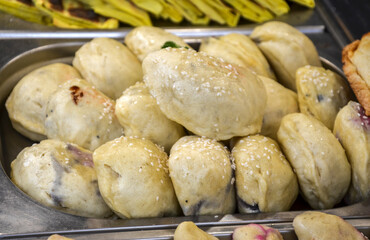 Metal tray is filled with numerous golden-brown dumplings, some of which are sprinkled with sesame seeds. The dumplings appear plump and ready to eat