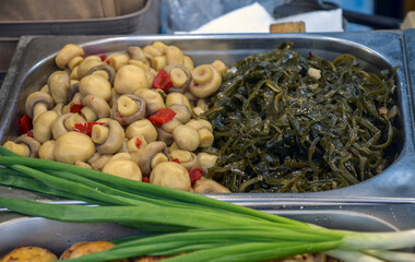 Marinated mushrooms and seaweed are presented in a stainless steel tray, showcasing colorful,...