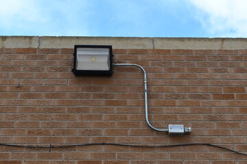 LED floodlight in alleyway. Electrical conduit runs to small junction box before disappearing into the building.