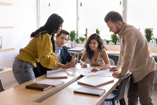 Group of four multiethnic workmates engaged in brainstorming session, reviewing data in documents and charts placed on table, working, thinking and analyzing together during corporate briefing event