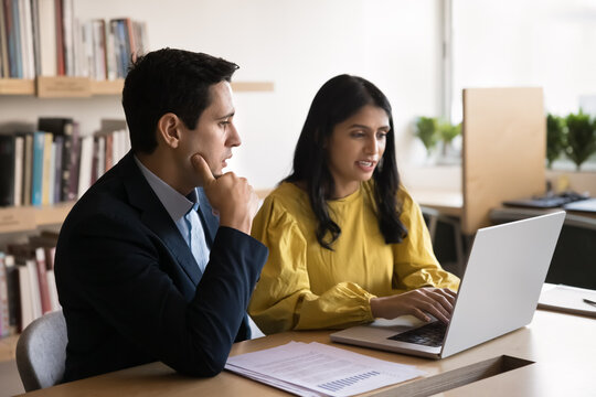 Indian woman using laptop presenting information to male colleague, analyzing or considering received statistical data, preparing presentation, working on joint task. Collaboration and productivity