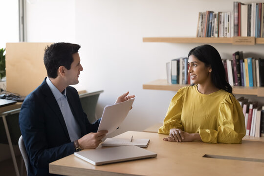 Attractive young Indian woman, vacancy applicant, answers questions during job interview sits at desk with male HR manager holding cv asking about education, qualification and competence. Recruitment