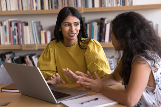 Two Indian workmates working together seated at desk with laptop, presenting concept or idea for new project, guiding or mentoring, collaborate, share strategy or solution, review business strategies