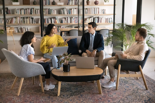 Group of four multinational professionals engaged in collaborative discussion, negotiations or brainstorming gather in cozy coworking office space. Teamwork, problem-solving, or strategy development