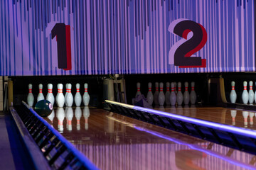 Bowling ball rolling toward pins on illuminated lane